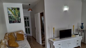 A living room with a sofa, a TV on a white cabinet, and a painting on the wall. - Nice apartment 8 minutes from la meynard hospital (Saint-Joseph 97212)