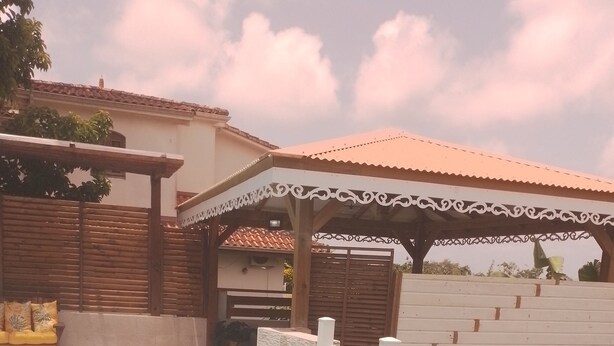 A swimming pool with a white fence, a covered seating area, and a building with a tiled roof. - Nice apartment 8 minutes from la meynard hospital (Saint-Joseph 97212)