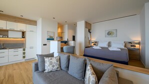 Een moderne hotelkamer met kitchenette, een bank met gestreepte kussens, een bed met netjes opgevouwen handdoeken en een minimalistische inrichting.