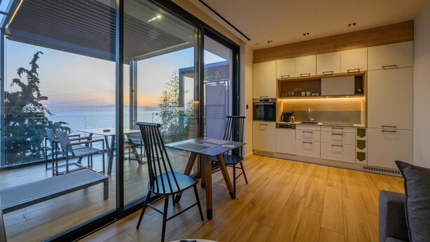 Een moderne keuken met uitzicht op zee, houten vloeren en een eethoek met stoelen.
