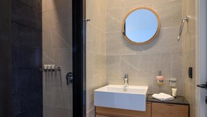 Een moderne badkamer met een douchecabine van glas, een witte wastafel en een ronde spiegel.