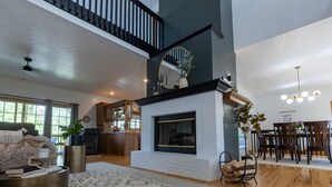 Un vaste espace de vie comprenant une cheminée, une table à manger et un escalier menant à l’étage supérieur.