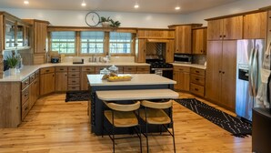 Une cuisine spacieuse avec des meubles en bois, un grand îlot central doté de tabourets, un réfrigérateur et une horloge au mur.