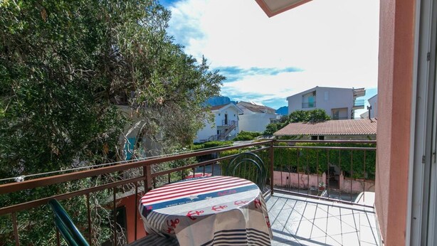 Un balcone con tavolo e sedie, affacciato su una zona residenziale con case e vegetazione.