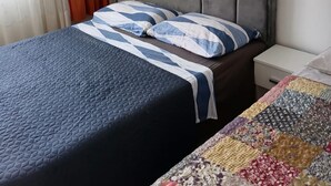 Un letto con una coperta blu e cuscini a righe, un comodino e una coperta colorata sul pavimento.