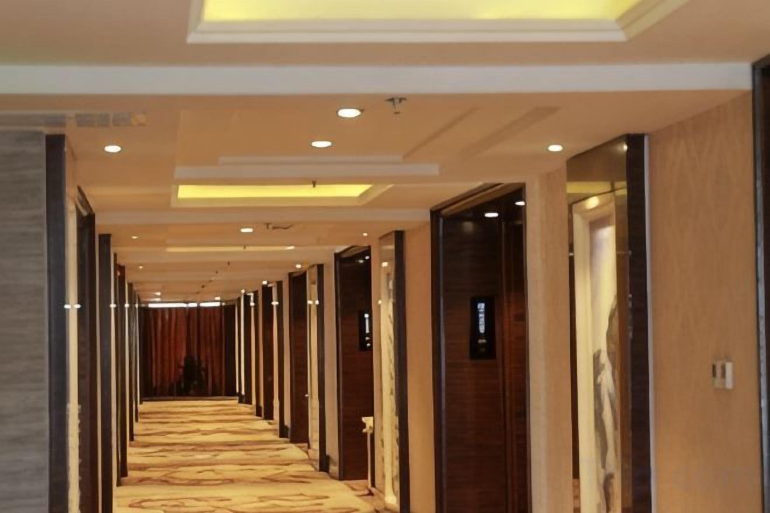 Un pasillo de hotel con puertas a ambos lados, iluminación empotrada y piso alfombrado.