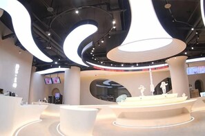 Un interno moderno con una piattaforma circolare centrale, diverse aree salotto e un grande schermo digitale.