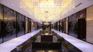 A hotel corridor with a reflective floor, a central water feature, and a large chandelier.