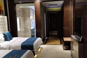 A hotel room with two beds, a TV, and a bathroom visible through a glass door. - Longchang Holiday Hotel (Tang County)