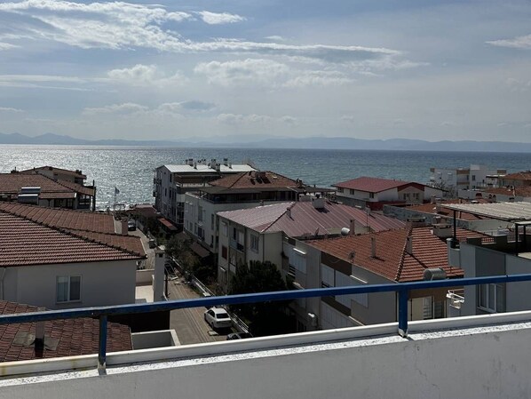Un área residencial costera con edificios de tejas rojas, vista despejada al mar y montañas al fondo.