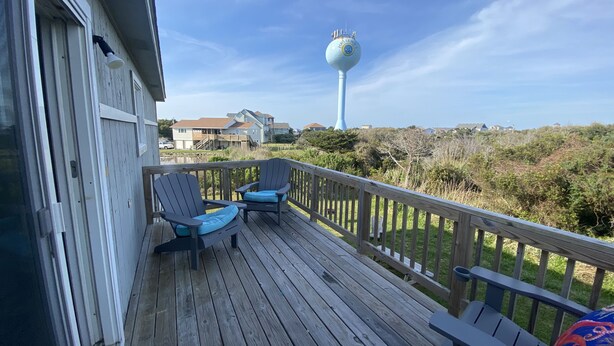 A wooden deck with two Adirondack chairs and a bench, overlooking a coastal area with houses and a tall blue tower. - Hatteras Village *** Southside 3 *** (Hatteras)