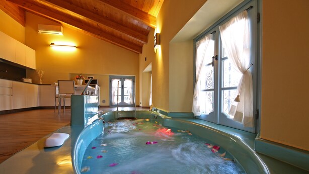 A spa area with a hot tub filled with water and rose petals, wooden ceiling beams, and a dining area in the background. - THE WAVE :: APARTMENT (Lezzeno)