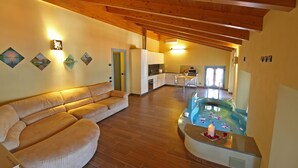 A spacious living area with a large beige sofa, a wooden ceiling, a kitchen area, and a hot tub with flower petals. - THE WAVE :: APARTMENT (Lezzeno)