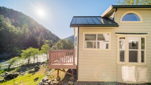 A house with a deck overlooking a river, surrounded by a forested hillside. - Strawhouse Resorts (Big Bar)