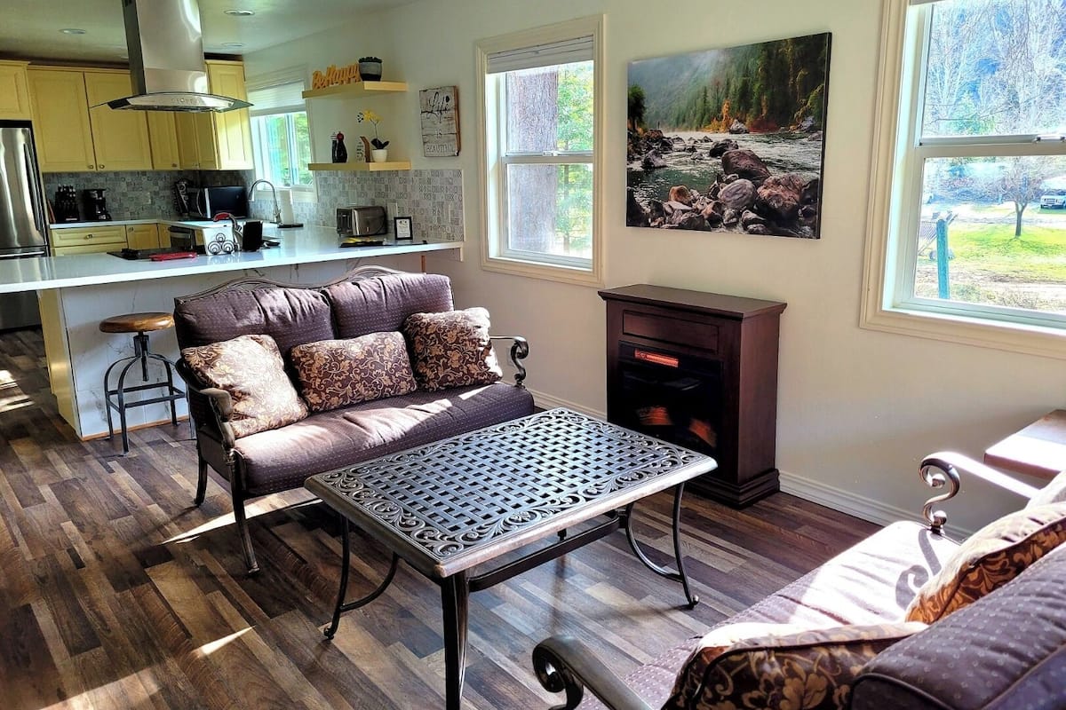 A modern kitchen with yellow cabinets, a built-in stove, and a dining area with a patterned sofa and metal table.