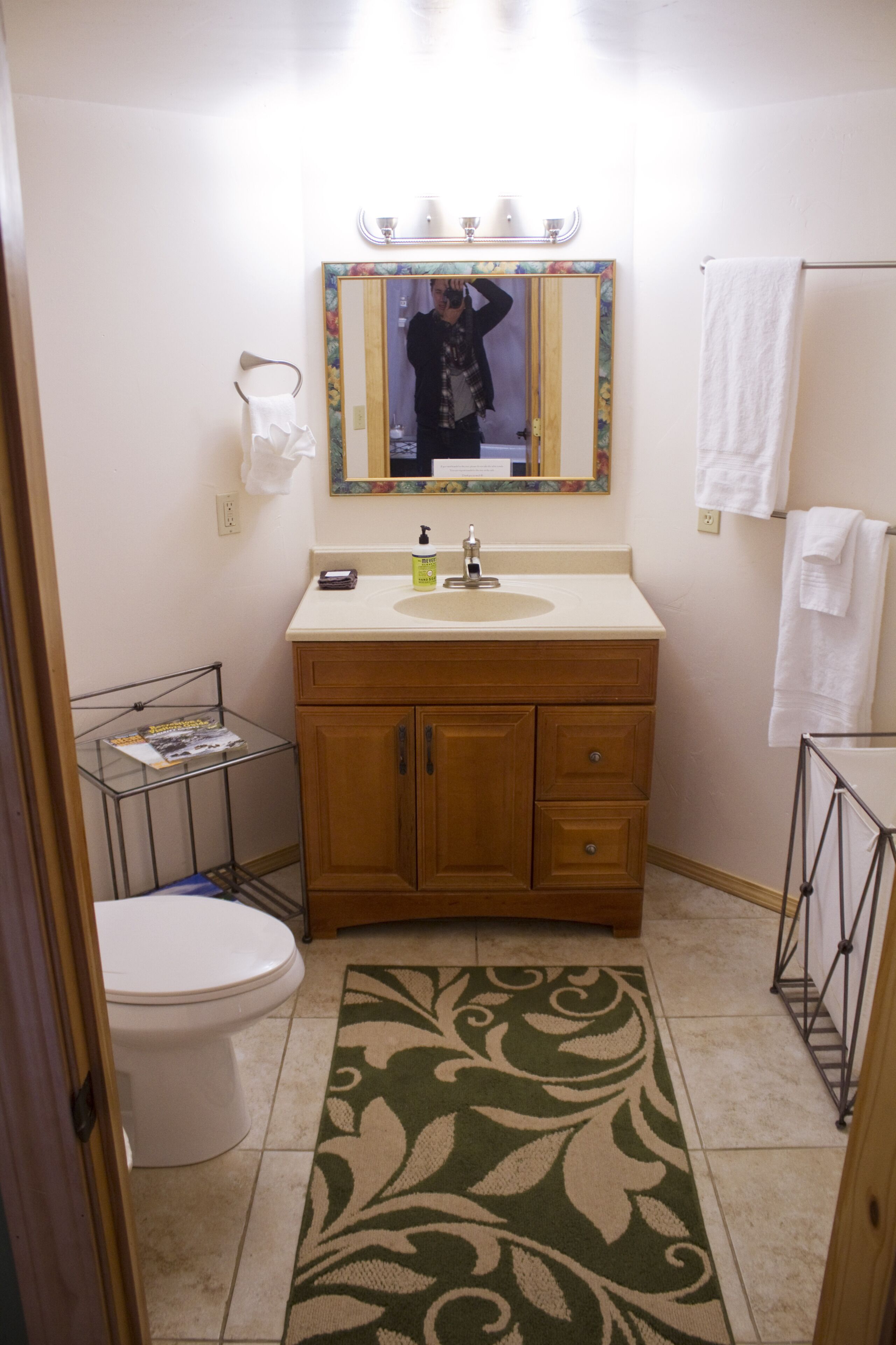 A bathroom with a toilet, sink, mirror, and a patterned rug.