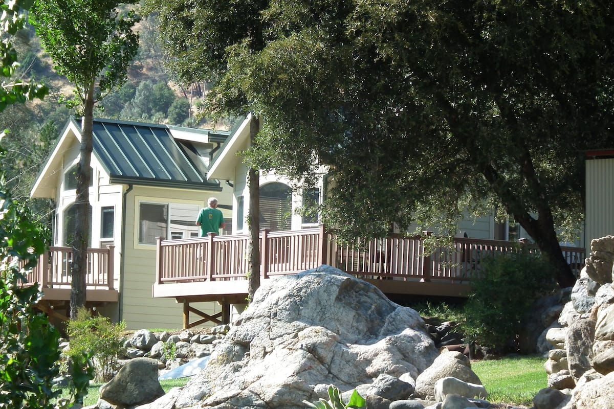 A two-story building with a balcony, surrounded by rocks and greenery.