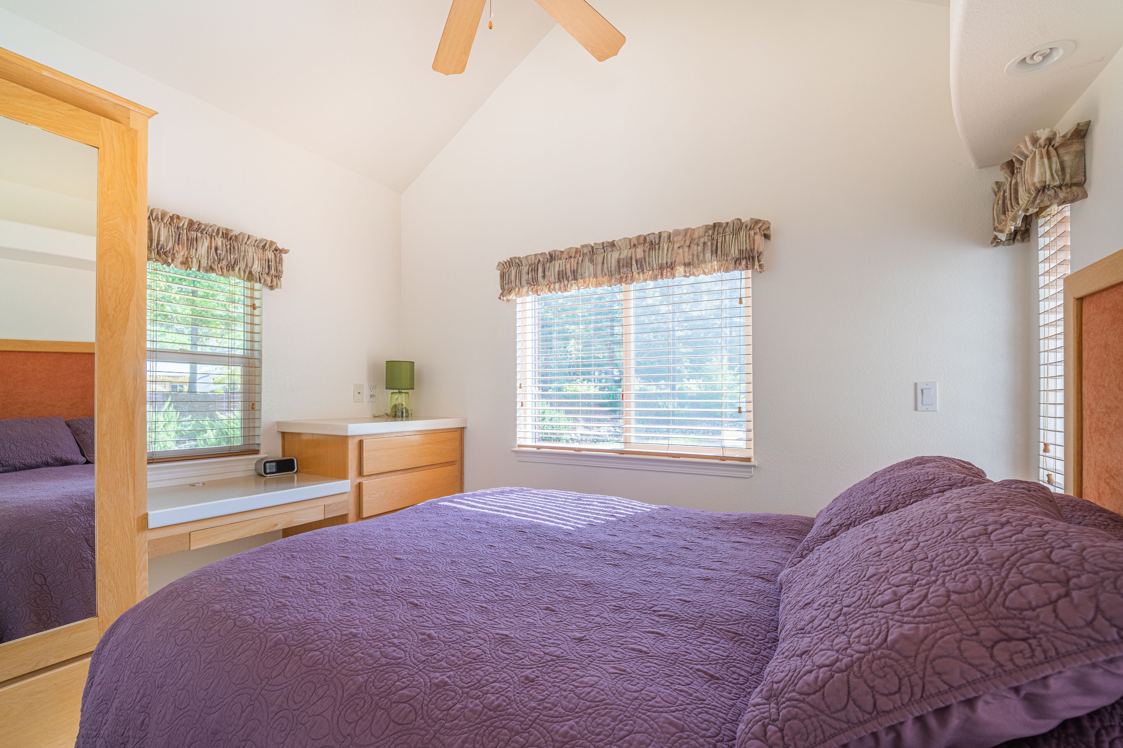 A bedroom with a large bed, a desk, and a window with blinds.
