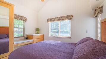 A bedroom with a large bed, a desk, and a window with blinds.