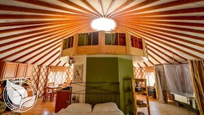 A yurt with a central light fixture, a bed, a table, and chairs. - Strawhouse Resorts (Big Bar)