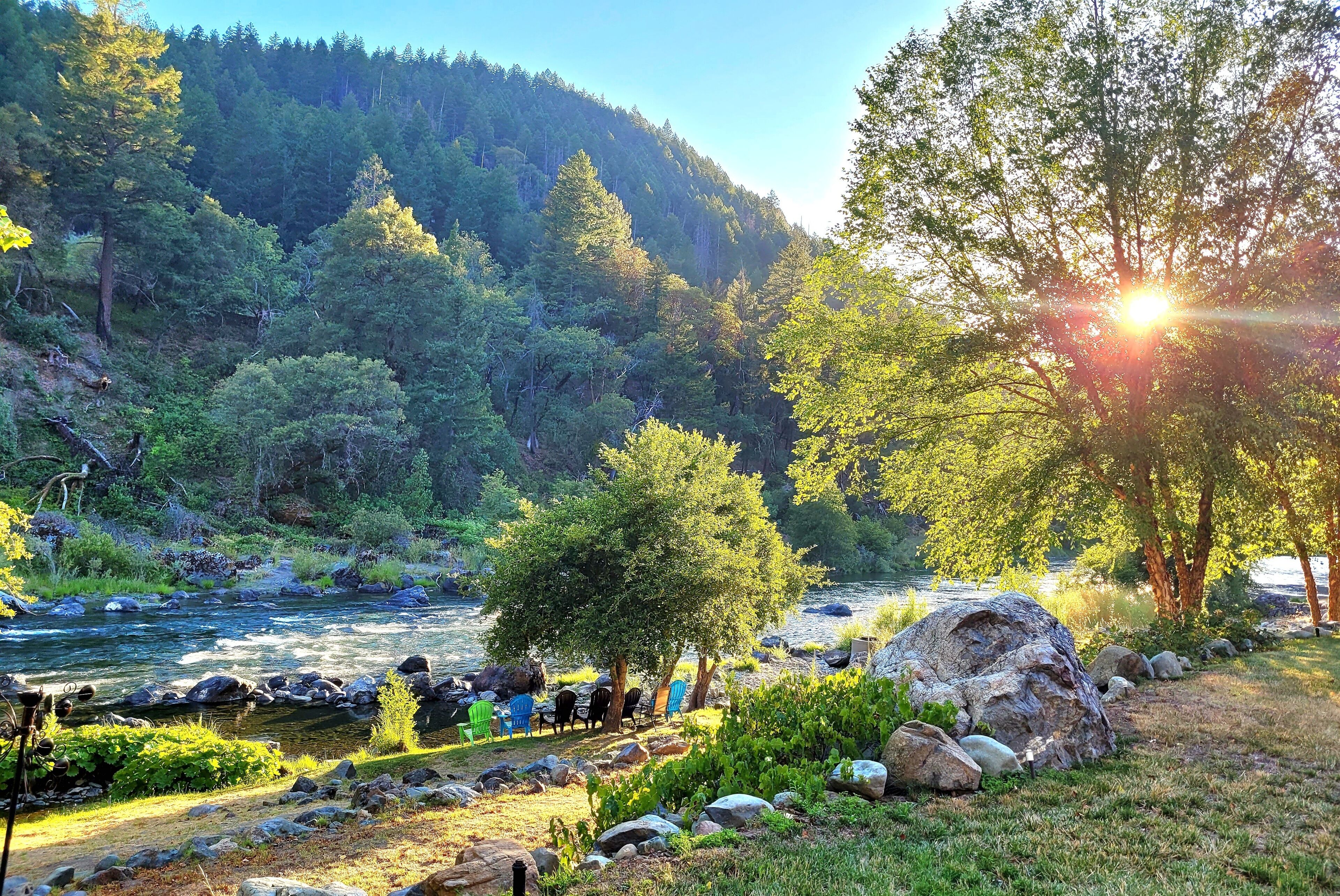 A riverside setting with a dining area, rocks, and trees.