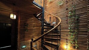 A spiral staircase in a wooden interior with bamboo walls and hanging plants. - A Good Year (Fenghuang County)