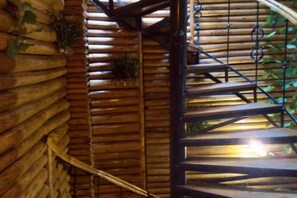 A wooden spiral staircase with metal railings, surrounded by wooden logs and greenery. - A Good Year (Fenghuang County)