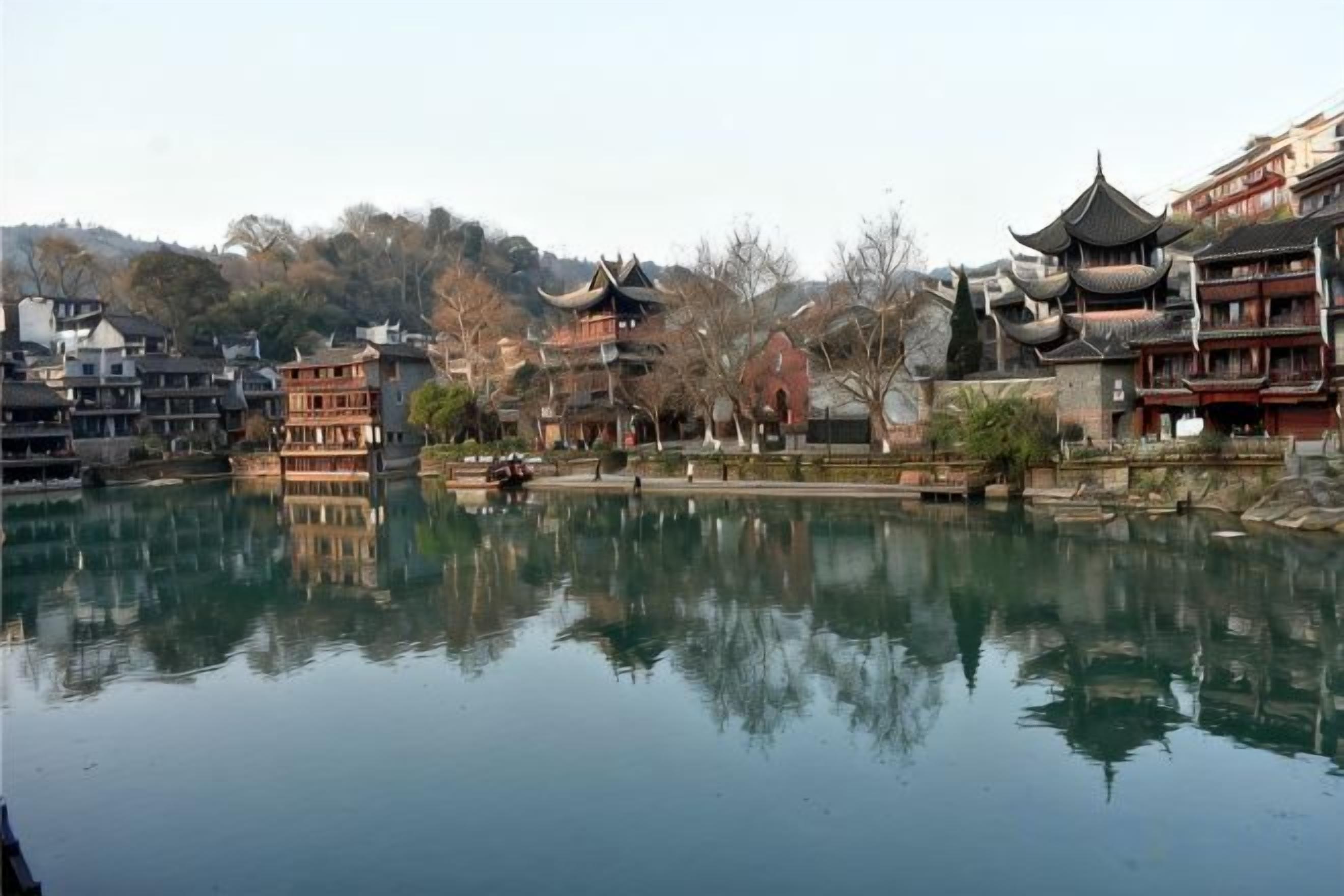 A traditional Chinese courtyard with buildings featuring tiered roofs and a calm water body reflecting the structures.