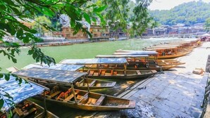 A row of traditional boats docked at a riverside pier with buildings in the background. - A Good Year (Fenghuang County)
