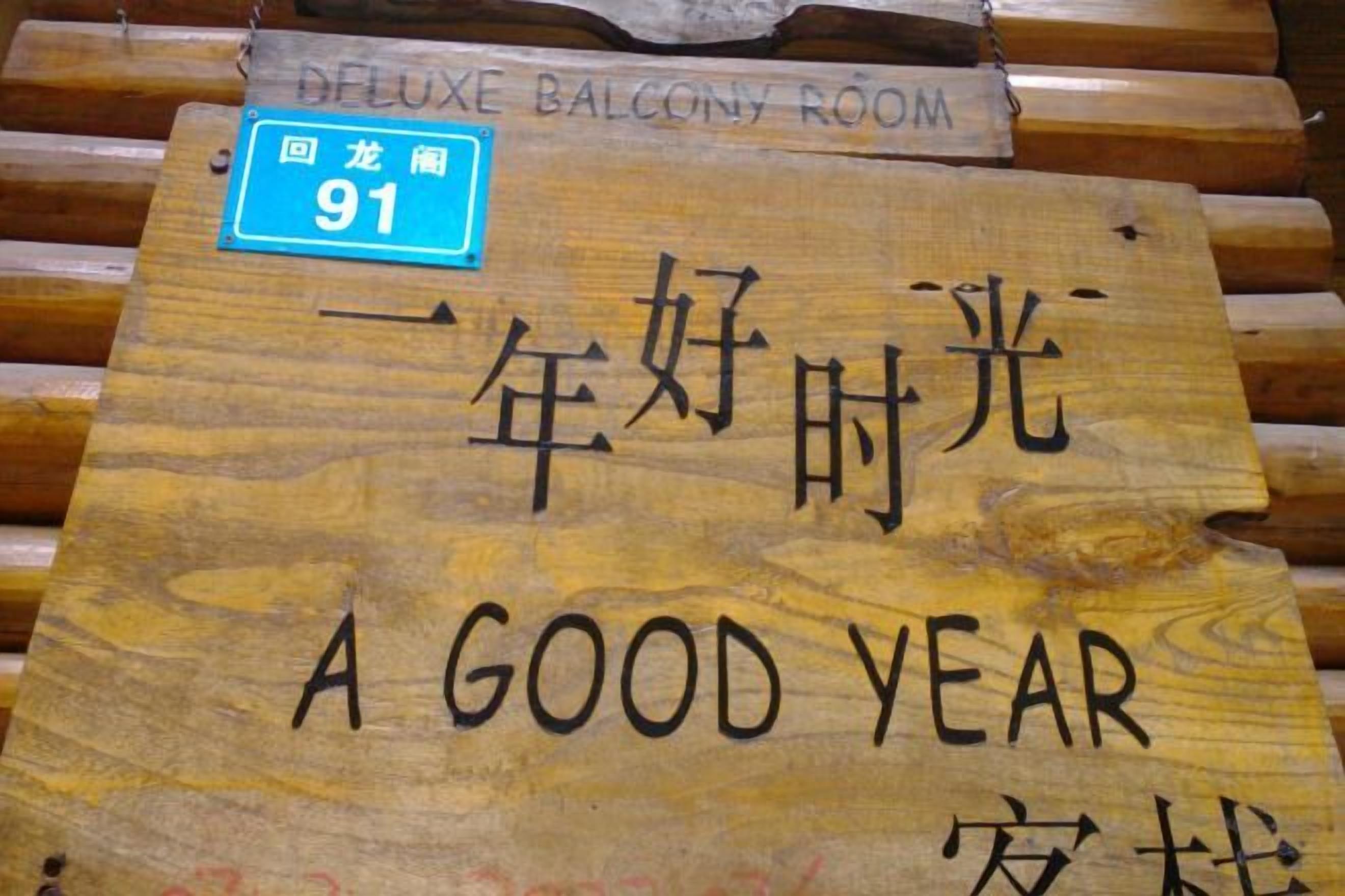 Un letrero de madera con el texto 'A GOOD YEAR' y 'Habitación Deluxe con Balcón', indicando el número de habitación 91.