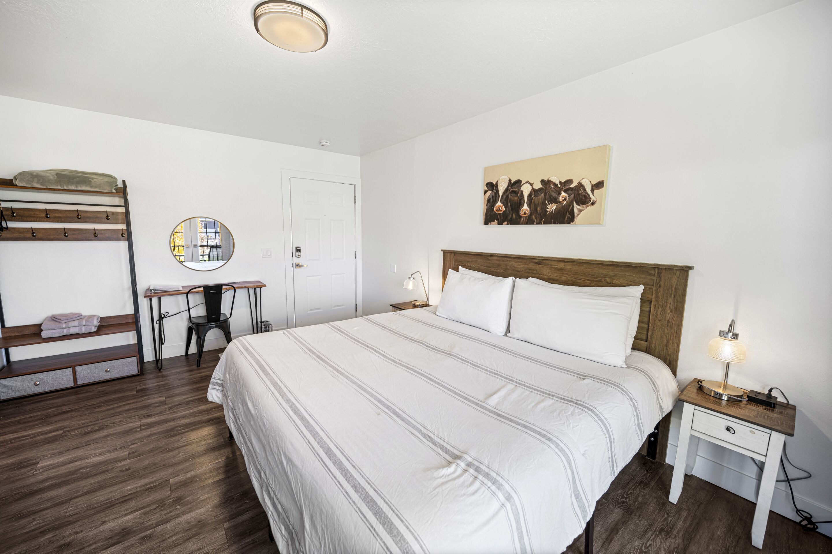 Une chambre à coucher avec un grand lit, un bureau, une chaise, un miroir et une œuvre d’art accrochée au mur.