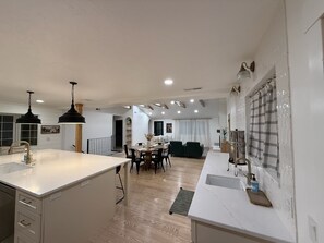 Una cocina moderna con una isla central, comedor y sala de estar con sofá y televisión.