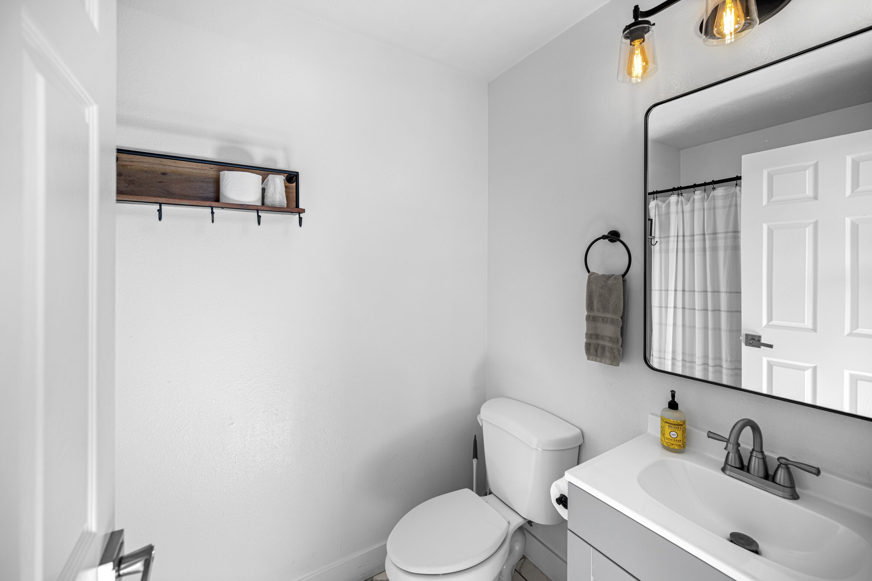 A bathroom with a white toilet, a white sink, and a mirror above the sink. There is a towel rack on the wall and a shelf above the toilet.