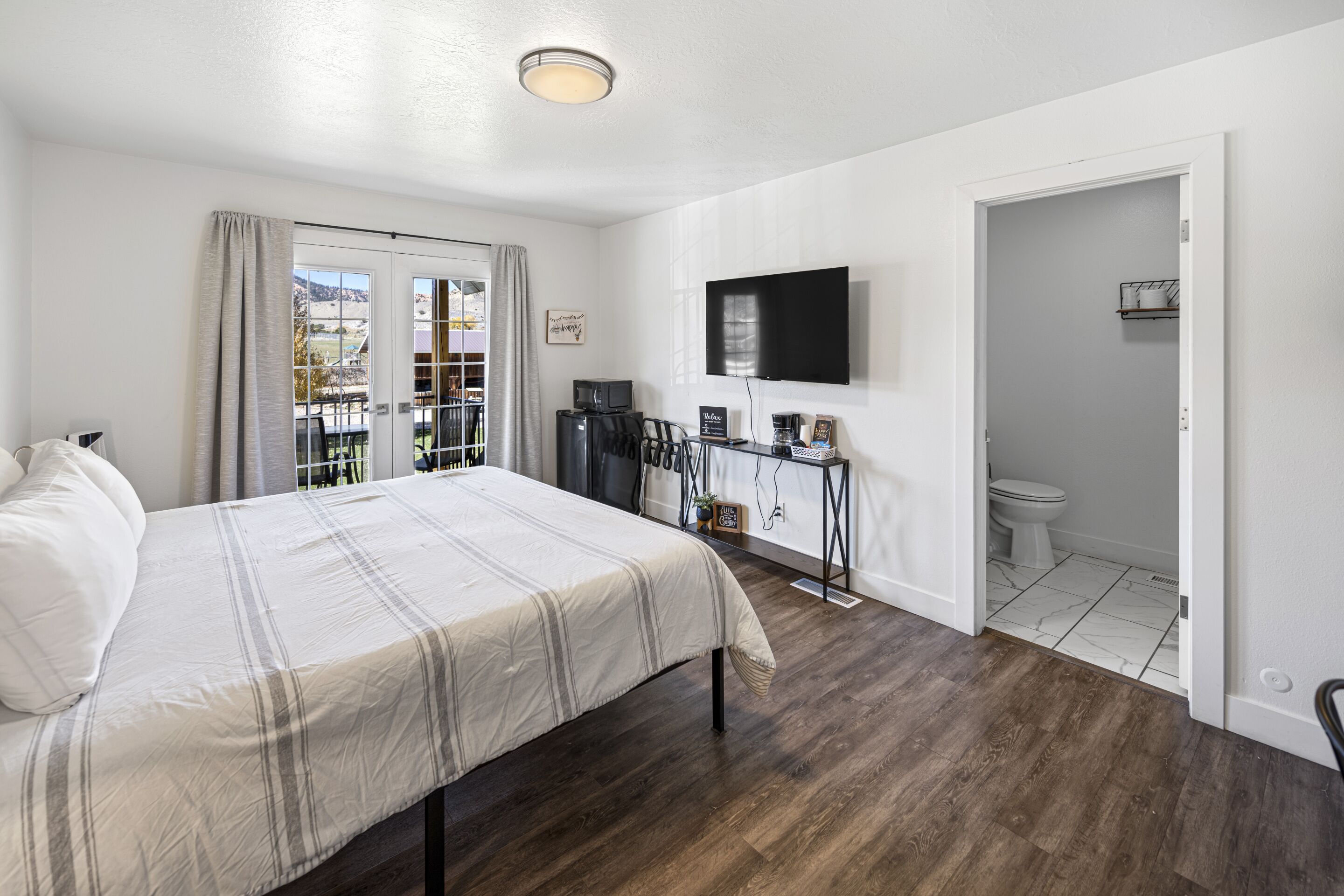 A bedroom with a bed, a TV, a desk with a computer, and a view of the outside.