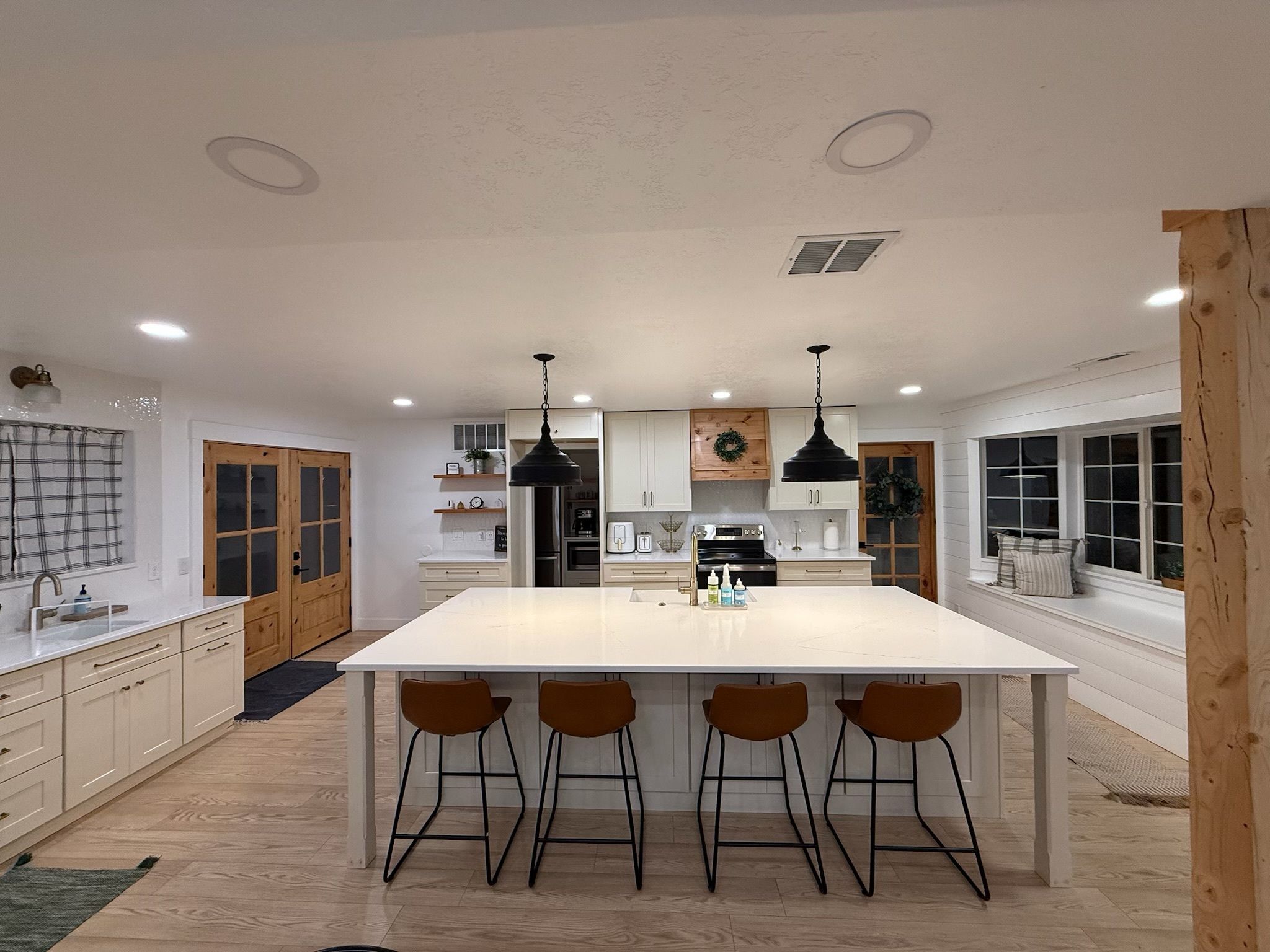 A modern kitchen with a central island, bar stools, pendant lights, and wooden cabinetry.