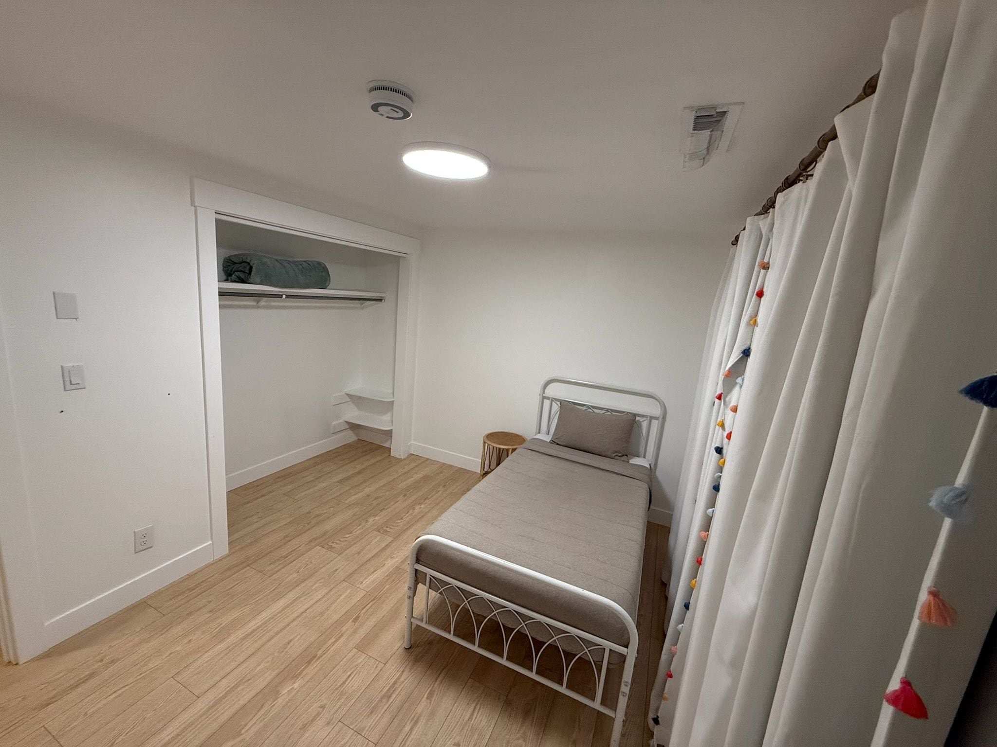 A bedroom with a bed, a wardrobe, a small table, and a ceiling light.