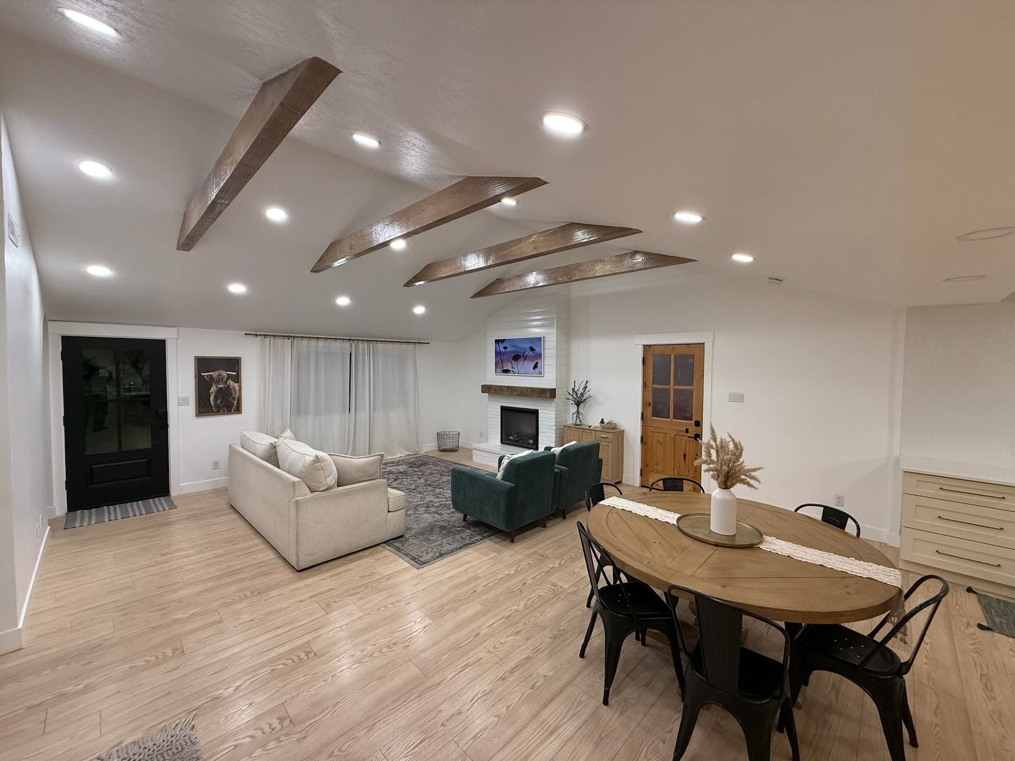 A modern living room with a sofa, a dining table with chairs, a fireplace, and a large window.