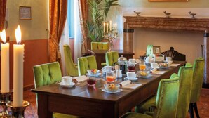 A dining room with a long table set for breakfast, green upholstered chairs, a fireplace, and a painting on the wall. - Vice King's Palace (Lezzeno)