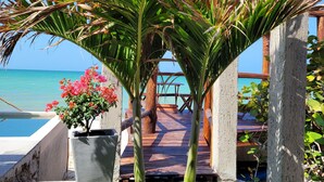 Eine Holzterrasse mit einem strohgedeckten Aufbau, einer Betonmauer und Blick aufs Meer.