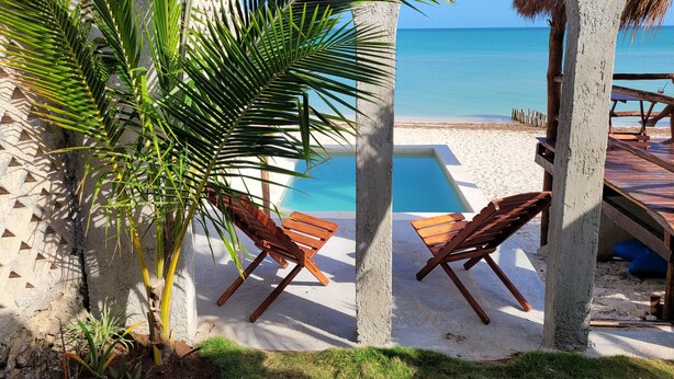 Ein Poolbereich am Strand mit Holzliegen und freiem Blick auf das Meer.