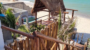 Eine Holztreppe führt zu einem Strandbereich mit einem Gebäude mit einem Reetdach.