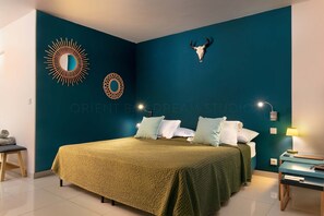 A bedroom with a bed, pillows, a wall-mounted mirror, a decorative skull, and a nightstand with a lamp.