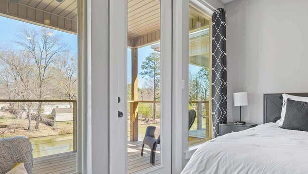 A bedroom with a bed, a nightstand, a chair, and a view of the outdoors through a sliding door. - Lakefront Gem in Lake Hamilton (Lake Hamilton)