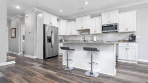 A modern kitchen with white cabinets, stainless steel appliances, and a central island with bar stools. - Lakefront Gem in Lake Hamilton (Lake Hamilton)