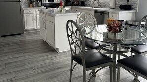 A modern kitchen with white cabinets, a central island, and a dining area with a glass table and metal chairs. - Cozy getaway in the Poconos — 5minutes away from all your favorite attractions ! (Stroudsburg)