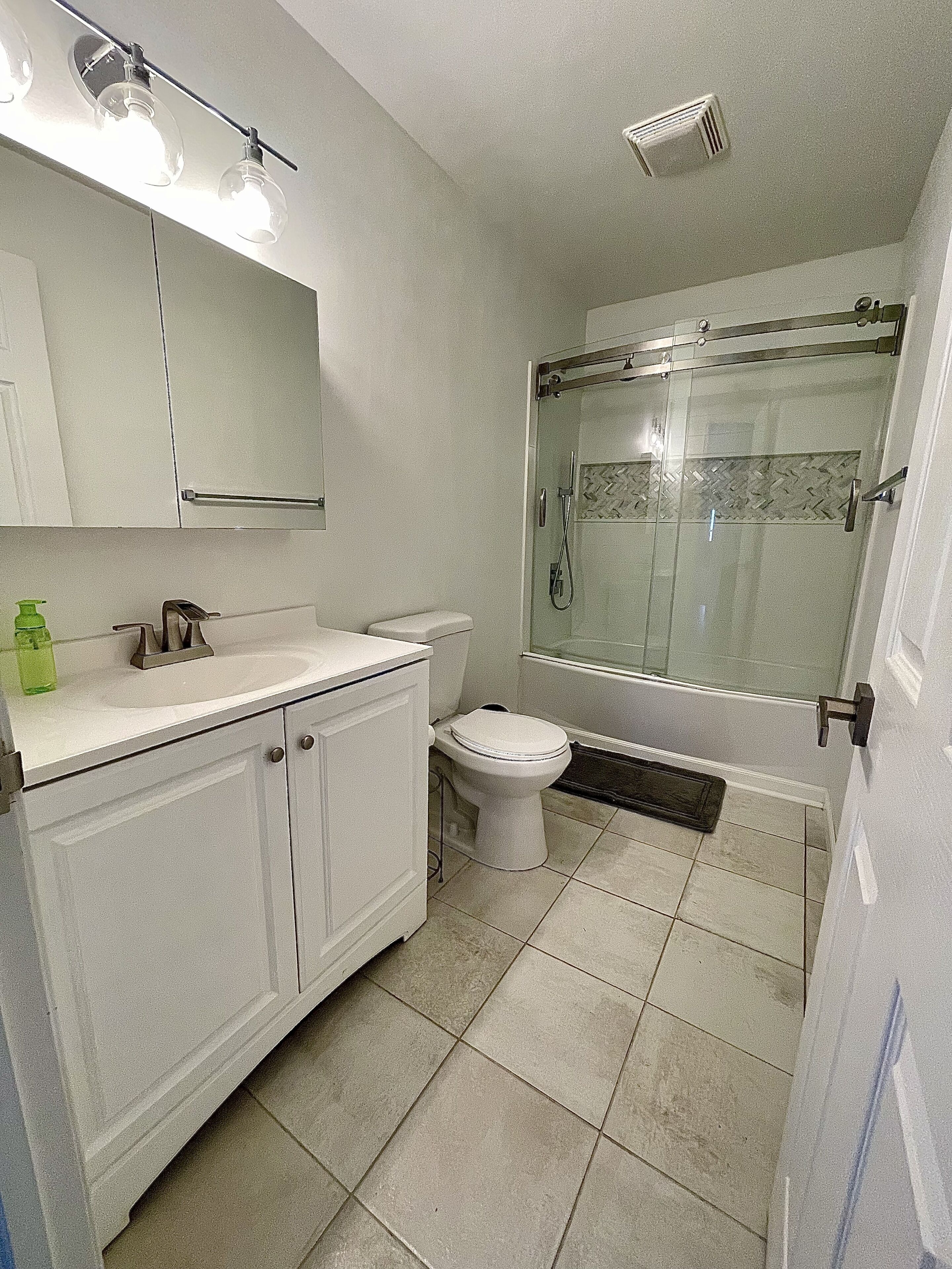 Un baño con lavamanos, espejo, inodoro y ducha blancos.
