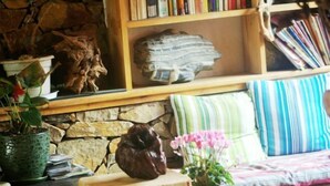 Un salón acogedor con una estantería de madera, una pared de piedra, un taburete de madera y un cojín a rayas.