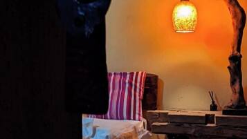 Une pièce faiblement éclairée, avec une table en bois, un coussin à rayures et un luminaire suspendu.