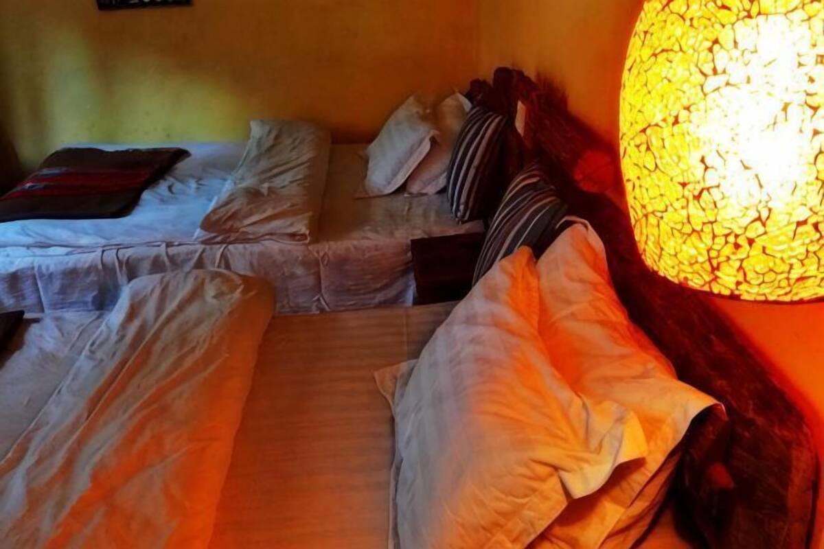 Quarto com duas camas, uma mesinha de cabeceira e uma luminária fixada na parede.