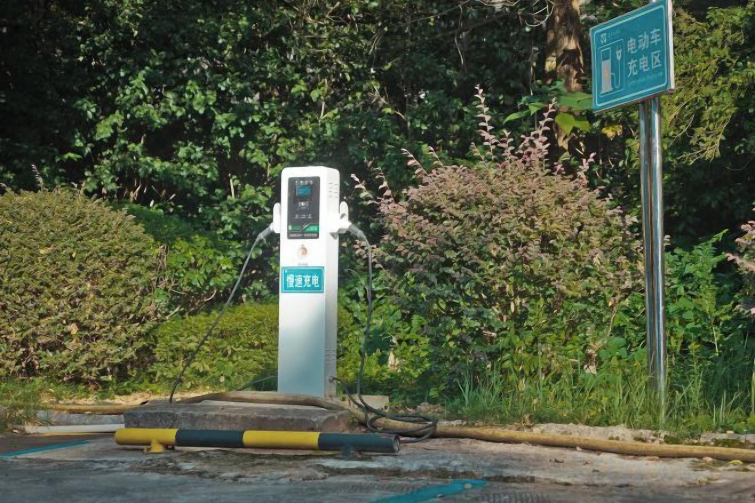 Estación de carga pública para vehículos eléctricos, con pantalla digital, rodeada de vegetación.